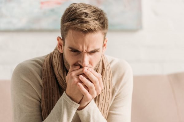 diseased man in warm scarf coughing in folded hands